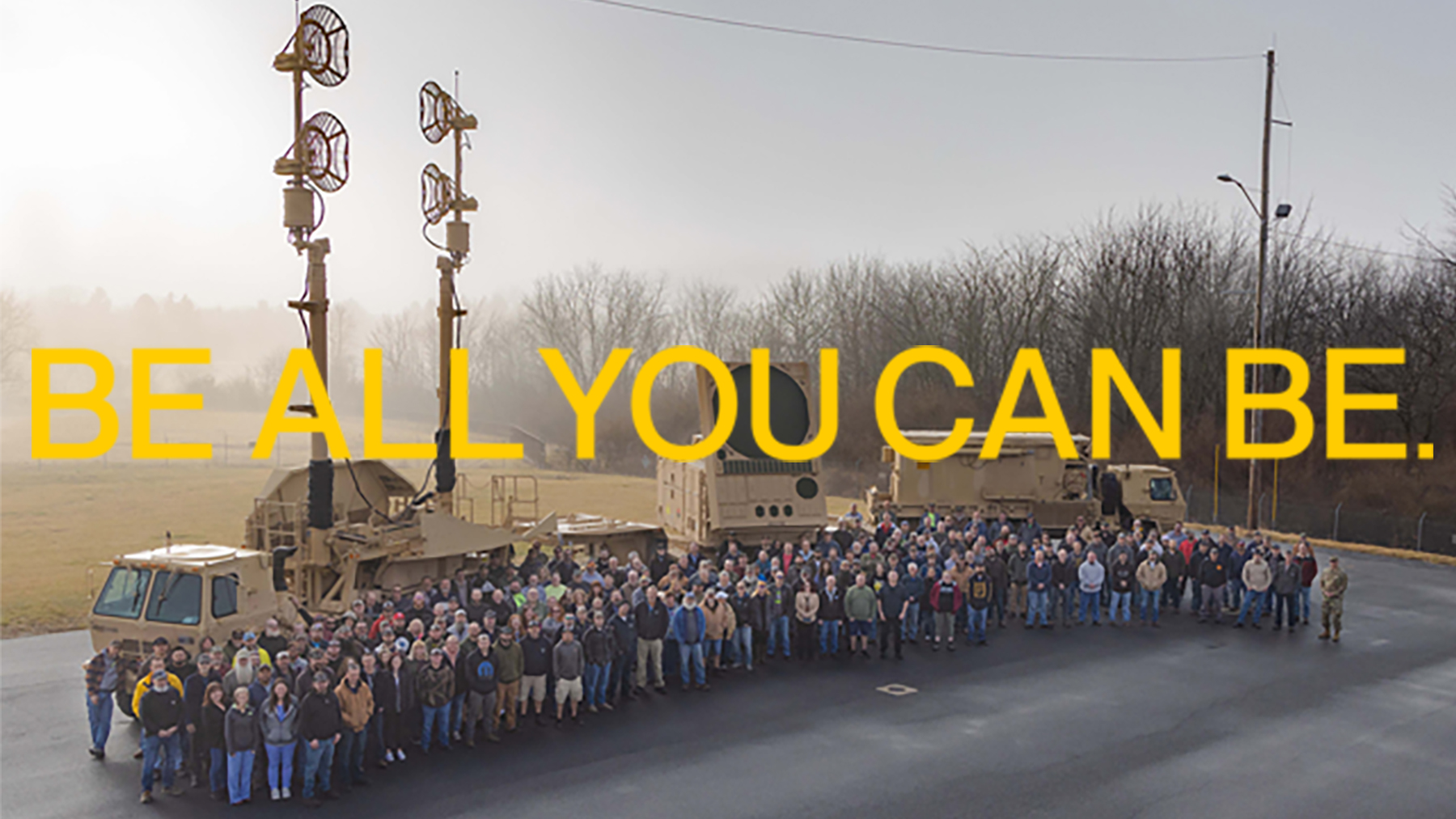 A group of workers stand in front of a PATRIOT System. The words 'Be All You Can Be' are superimposed on the image
